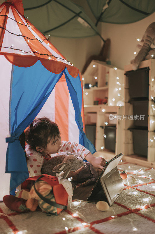 asian chinese child playing in the playroom in the tent using digital tablet lying down